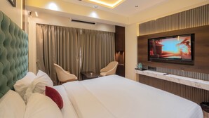 A hotel room with a bed, two chairs, a television, and a ceiling fan. - Mosaic Go Star Grand (Navi Mumbai)