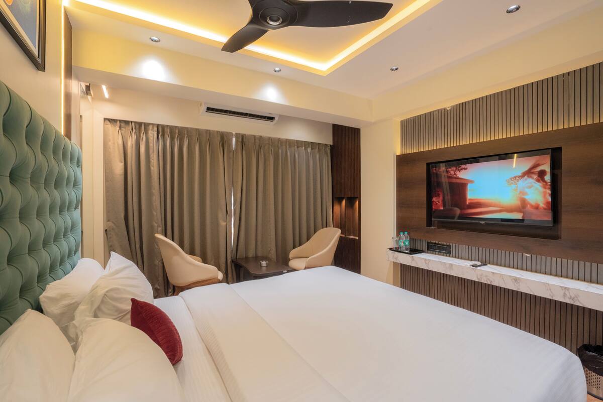 A hotel room with a bed, two chairs, a television, and a ceiling fan.