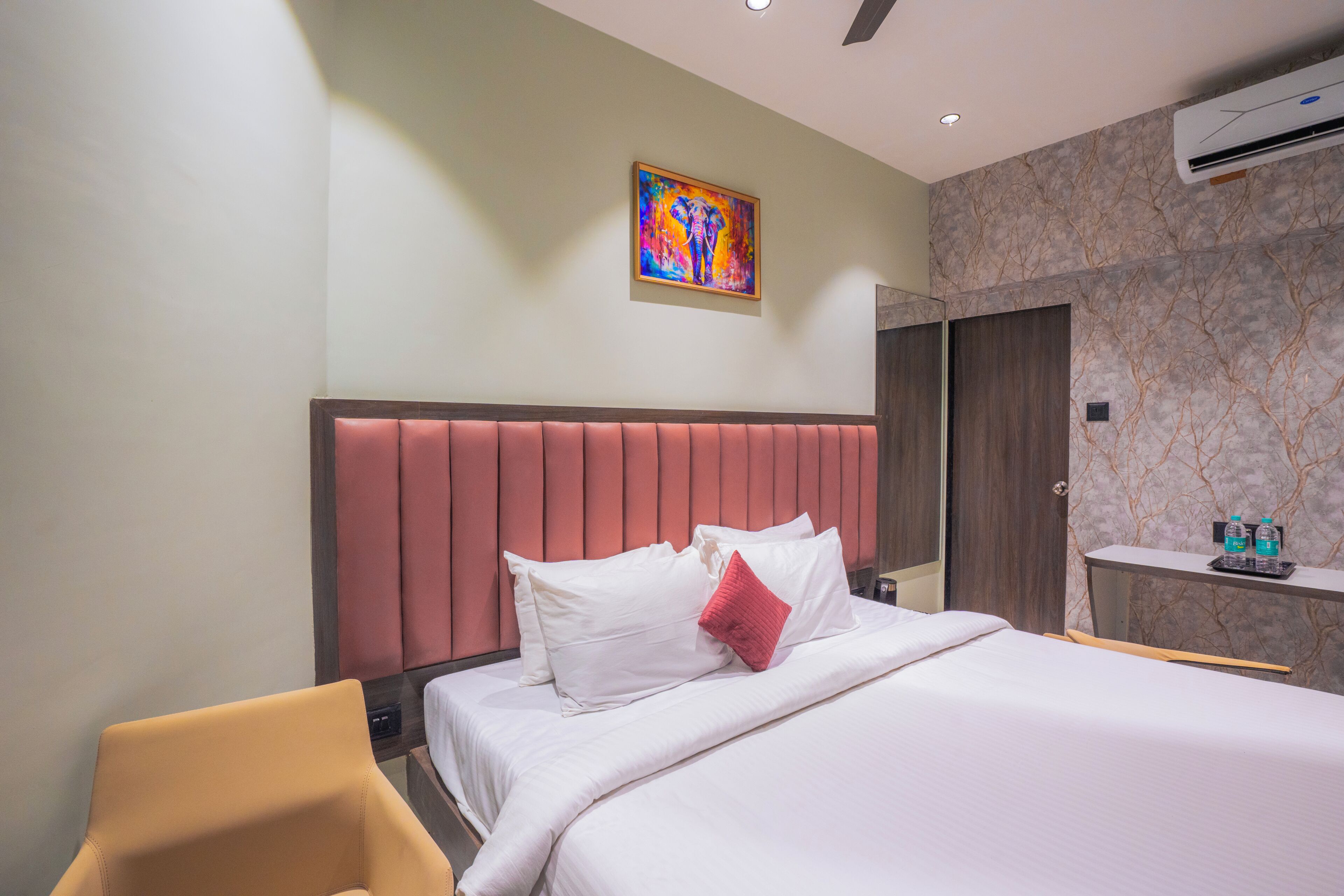 Una habitación de hotel con una cama, una silla, un cuadro en la pared y una mesita con botellas de agua.