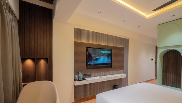 A hotel room with a bed, a TV mounted on the wall, a seating area, and a wooden panel design. - Mosaic Go Star Grand (Navi Mumbai)