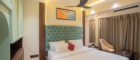 A hotel room with a large bed, a ceiling fan, a painting, a desk, and a chair.