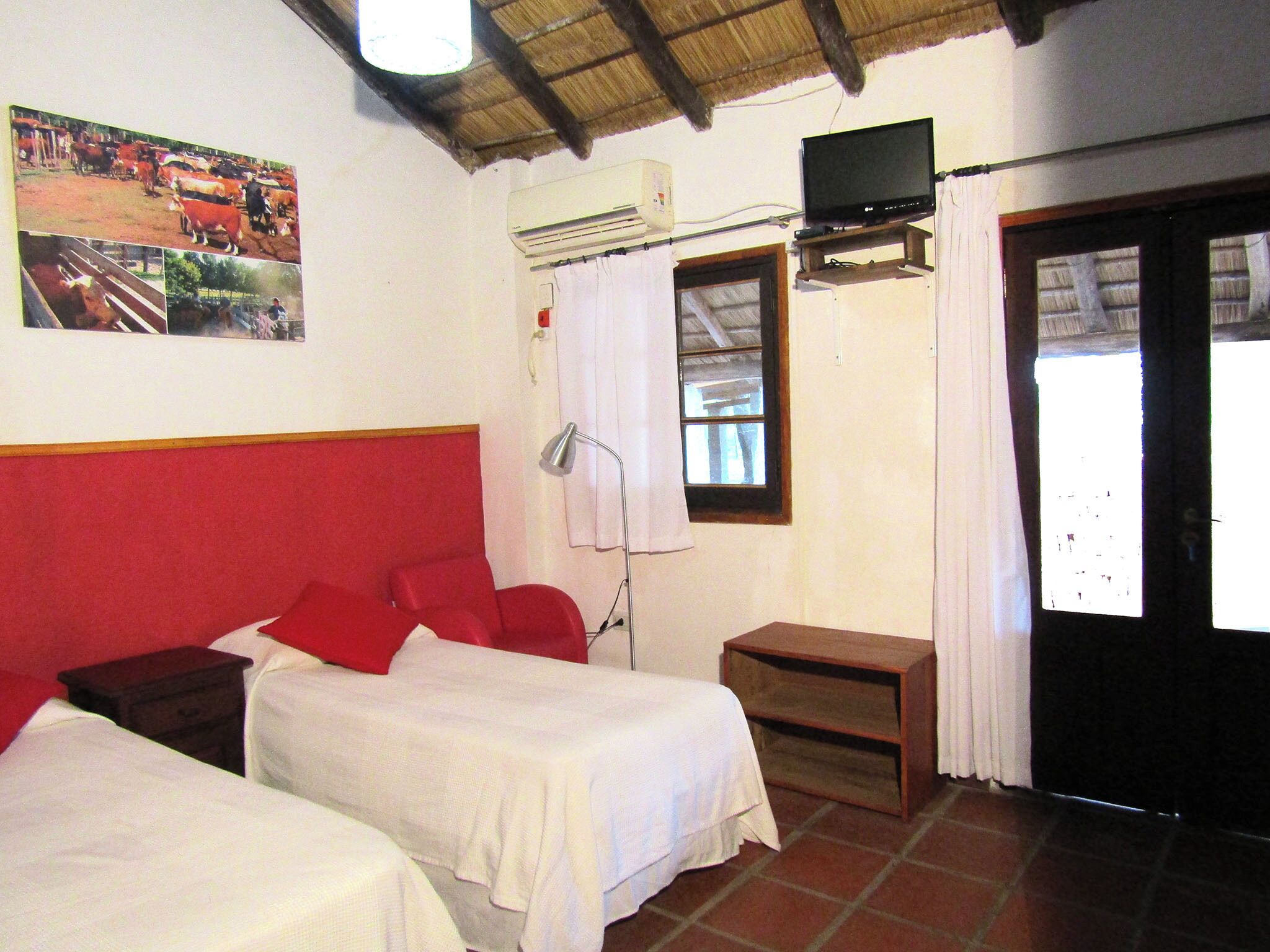 A room with two beds, a TV, an air conditioner, a window with curtains, and a door.