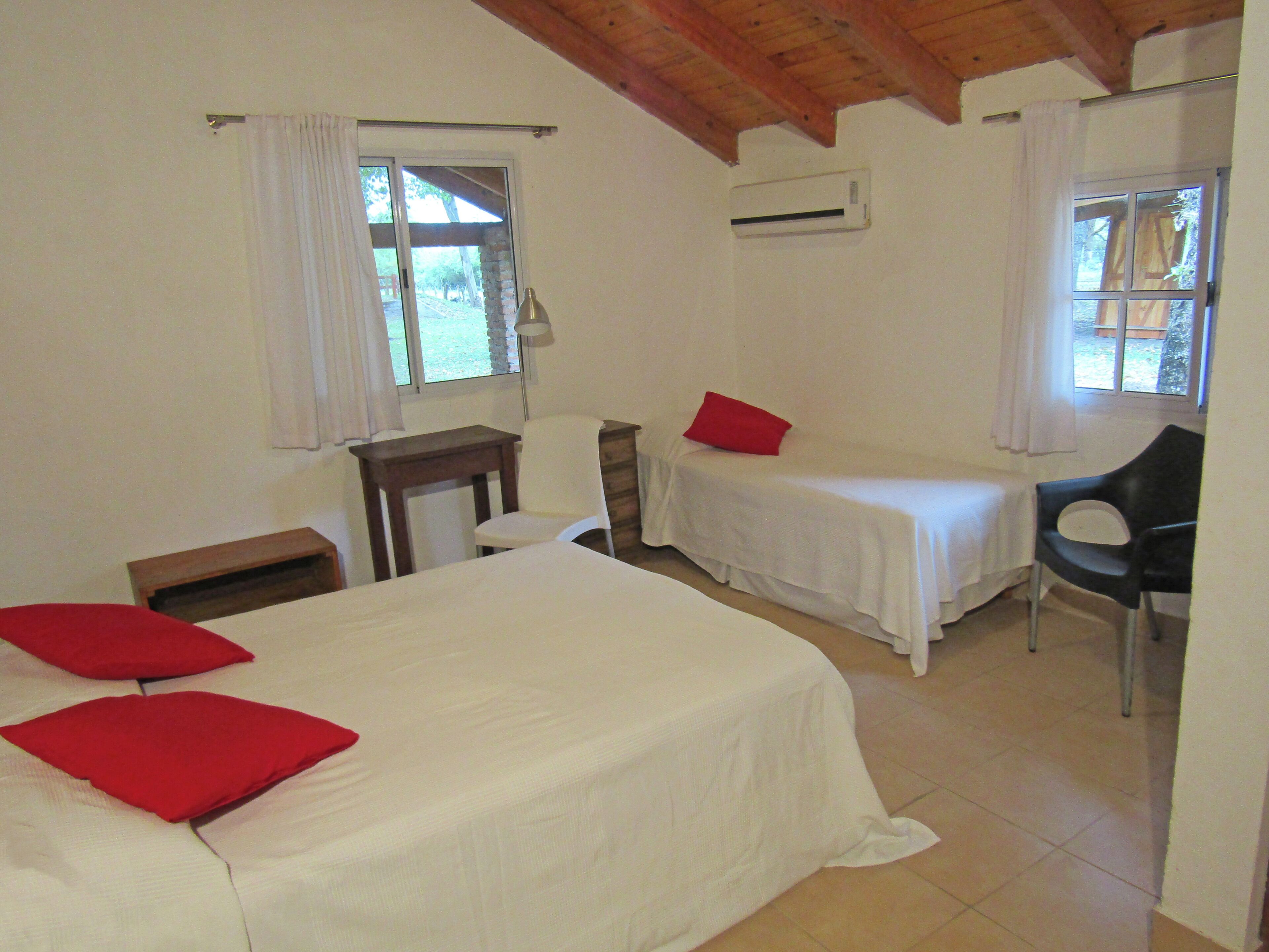 A room with two single beds, a desk, a chair, and an air conditioning unit.