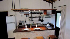 Une cuisine avec un îlot central en bois, un réfrigérateur, une cuisinière et des ustensiles de cuisine suspendus.