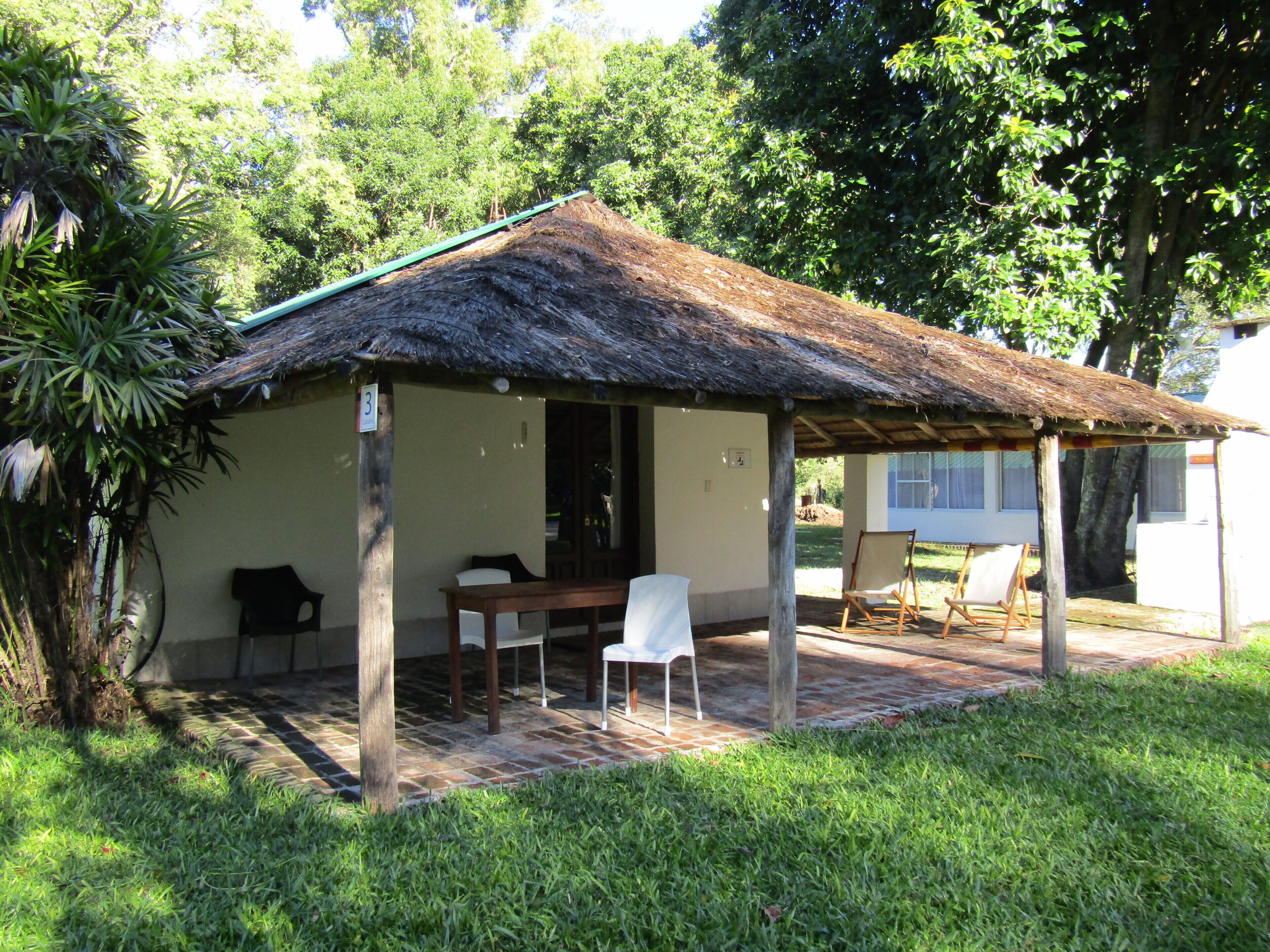 A small, single-story structure with a thatched roof, a table, and two chairs.