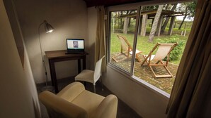 Une pièce comprenant un bureau, un ordinateur portable, une chaise et donnant sur un espace extérieur aménagé avec des chaises et des arbres.