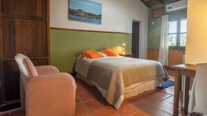 Une chambre à coucher avec un lit, une chaise, une table de chevet, une fenêtre avec des rideaux et un tableau au mur.