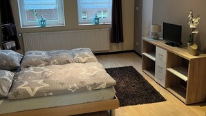 Makuuhuoneessa on sänky, työpöytä, televisio ja kaksi ikkunaa, joissa on verhot.