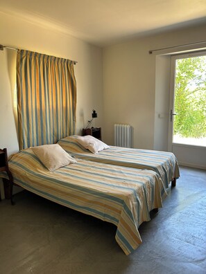 Un dormitorio con dos camas, un radiador, una ventana con cortinas y una mesita de noche con lámpara.
