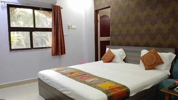 A bedroom with a bed, a window with curtains, an air conditioning unit, and a patterned wall. - HOTEL VAIDYA REGENCY (Balaghat)