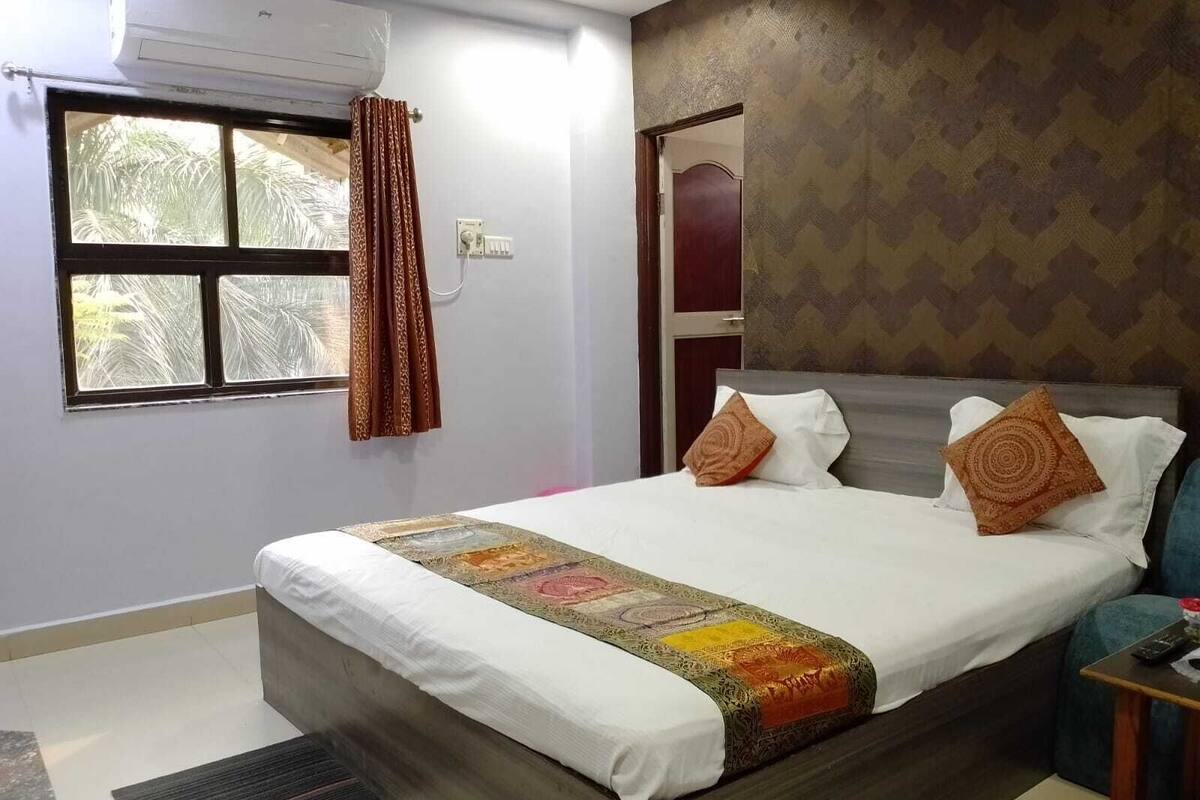 A bedroom with a bed, a window with curtains, an air conditioning unit, and a patterned wall.