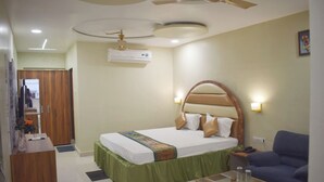 A hotel room with a bed, a desk, a chair, a ceiling fan, an air conditioning unit, and a wall-mounted light. - HOTEL VAIDYA REGENCY (Balaghat)