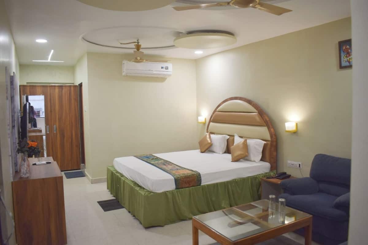 A hotel room with a bed, a desk, a chair, a ceiling fan, an air conditioning unit, and a wall-mounted light.