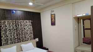 A hotel room with a bed, a nightstand, a mirror, and a wall-mounted light fixture. - HOTEL VAIDYA REGENCY (Balaghat)
