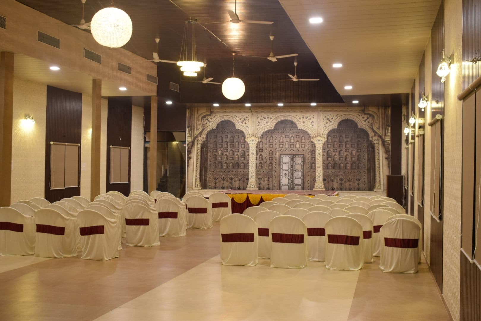 Uma sala de conferências com fileiras de cadeiras, um palco e uma parede decorativa.