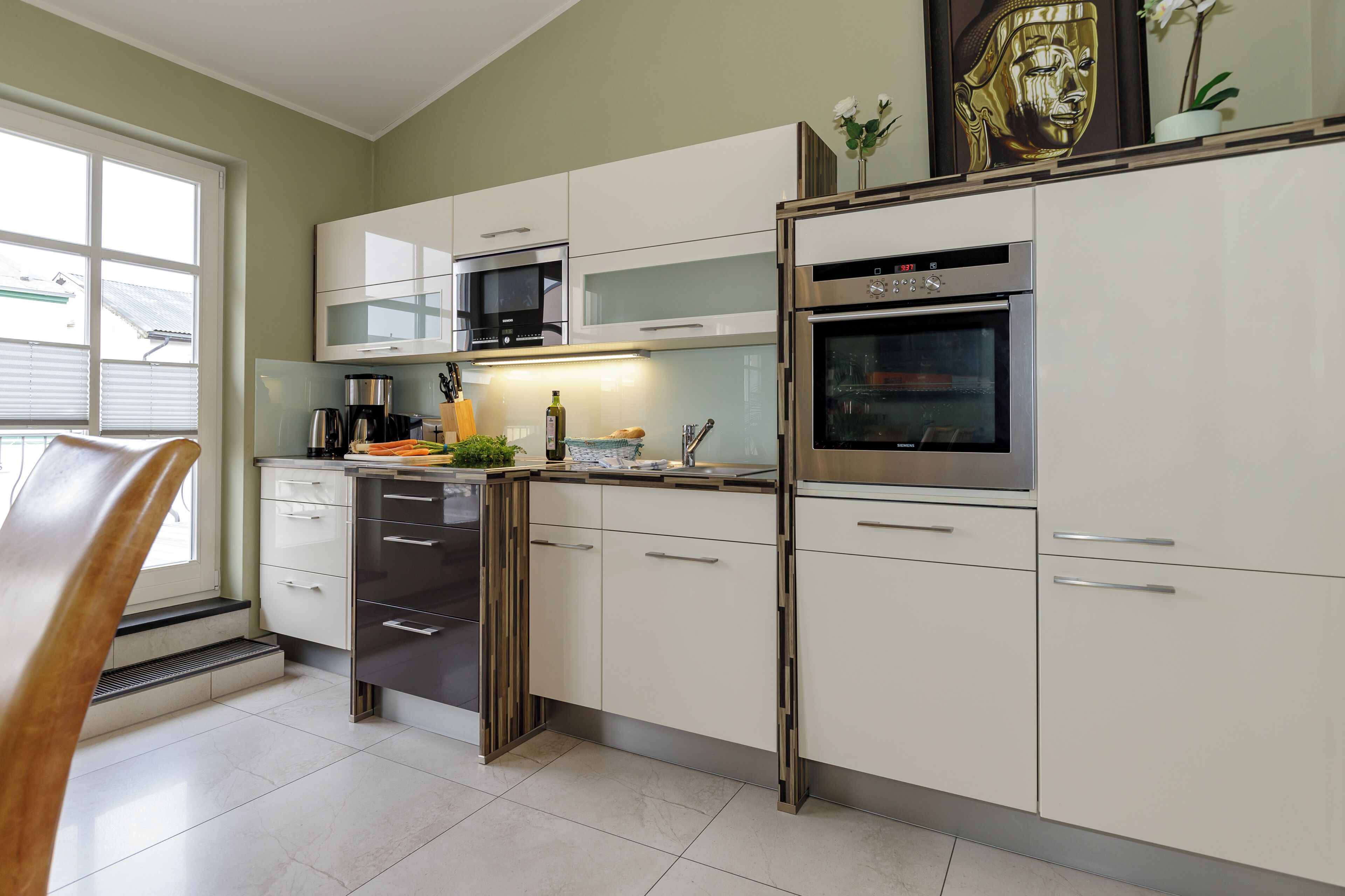 Una cocina moderna con electrodomésticos de acero inoxidable, armarios blancos y un ventanal que proporciona luz natural.