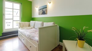 Una habitació amb un llit, una finestra, un quadre penjat a la paret i una planta en test.