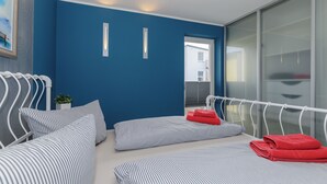 Habitació d'hotel moderna amb una paret d'accent blau, un llit blanc amb roba de llit a ratlles, un coixí vermell i una finestra gran.