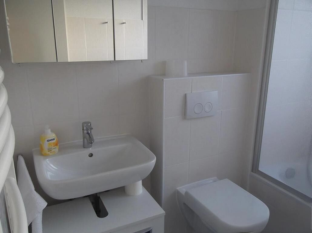 Un baño con lavamanos, inodoro y muebles blancos.
