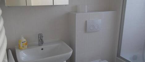 Un baño con lavamanos, inodoro y muebles blancos.