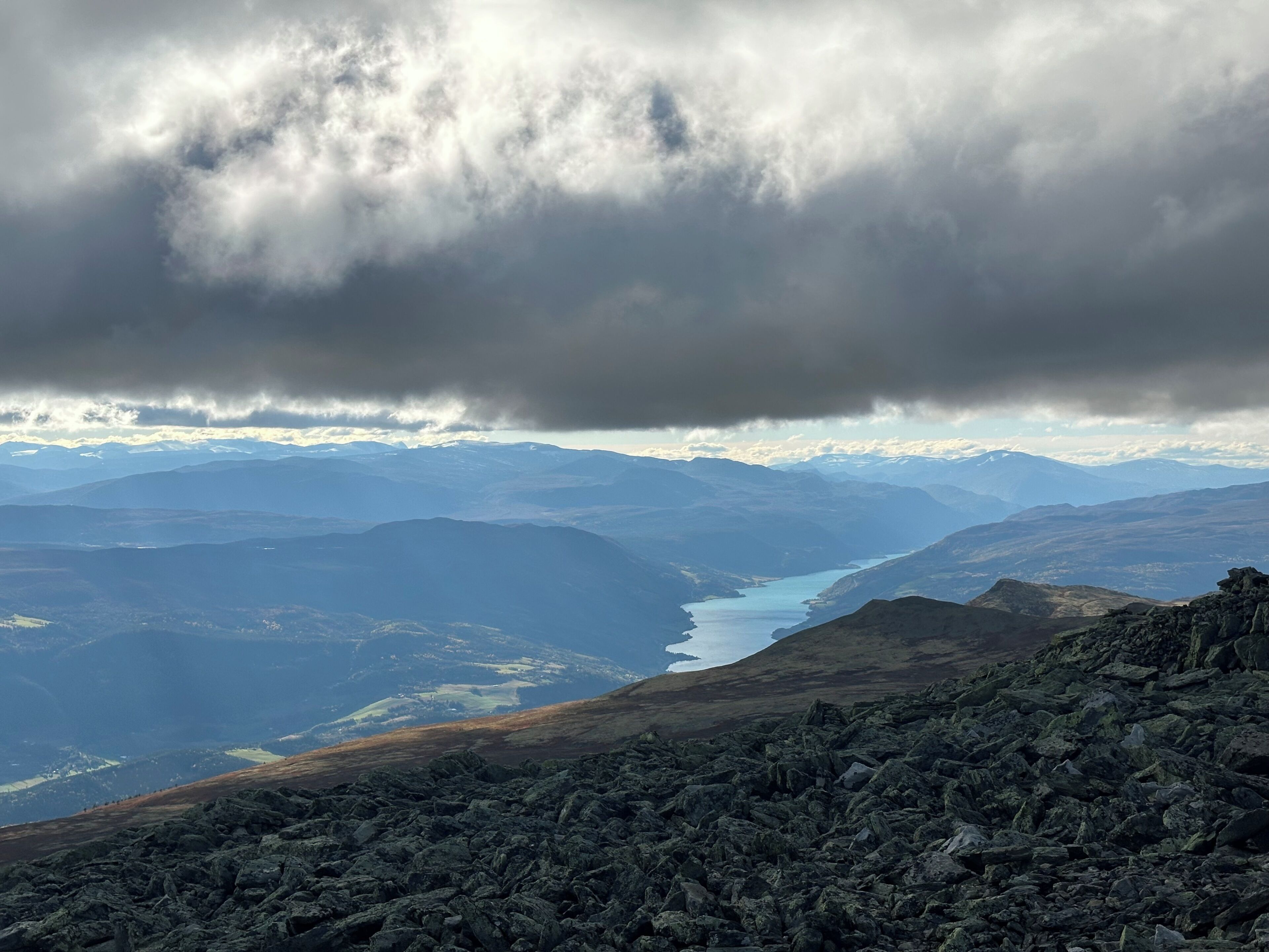 A mountainous landscape with a river, rocky terrain, and distant snow-capped peaks.