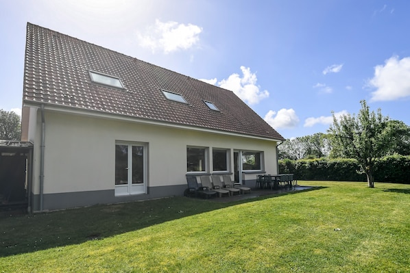 A two-story house with a tiled roof, large windows, and a grassy yard.