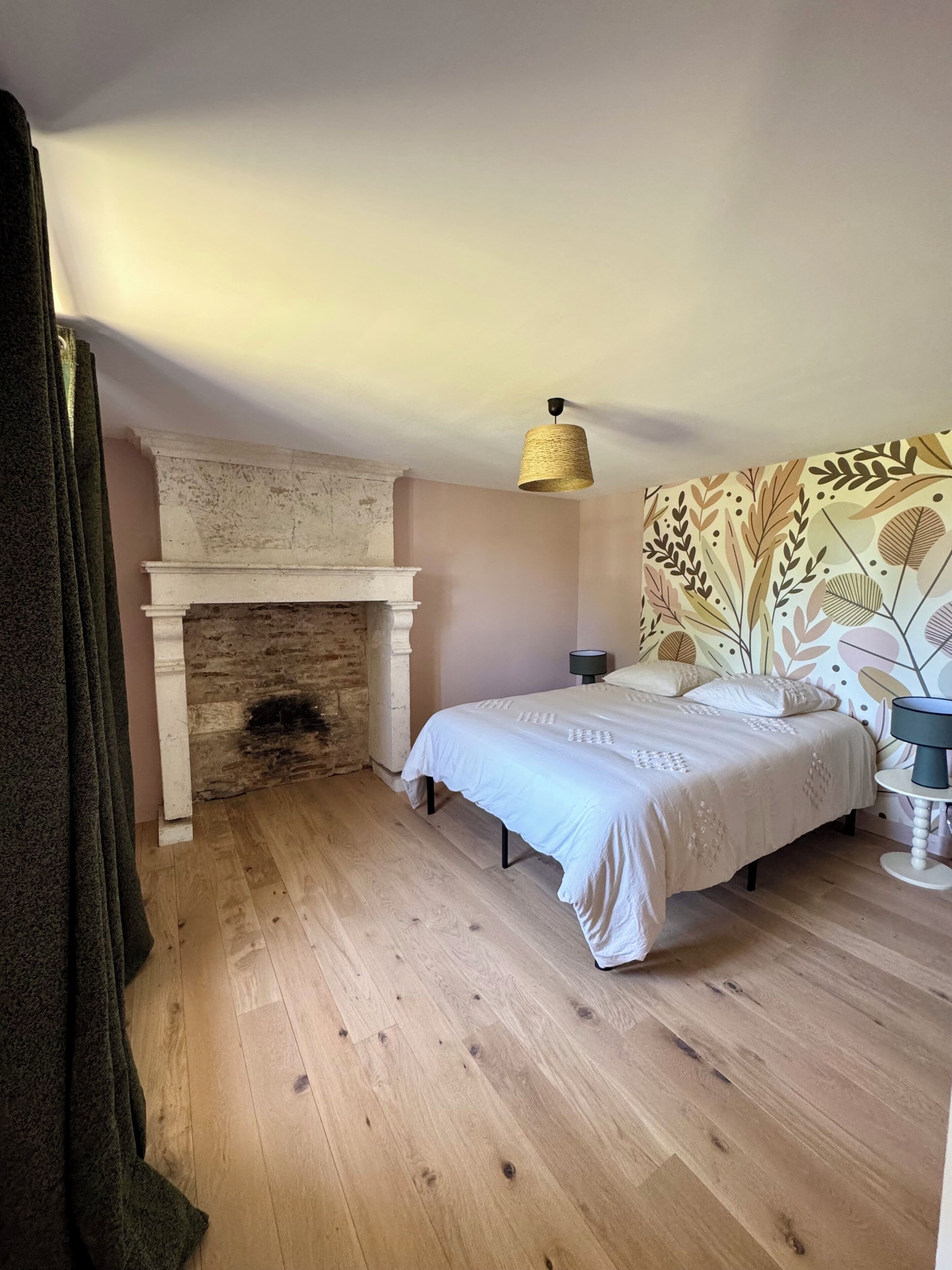Ein Schlafzimmer mit Kamin, Bett, Nachttisch, Lampe und Wand mit Muster.