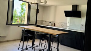 Eine moderne Küche mit einem Holztisch, schwarzen Stühlen, einer schwarzen Dunstabzugshaube und einem Fenster mit Blick auf Bäume.