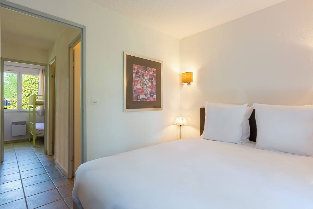 A hotel room with a bed, a painting on the wall, a lamp, and a view of a balcony.