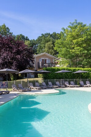 A swimming pool with lounge chairs and umbrellas, surrounded by greenery and a building in the background.