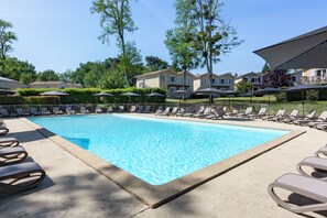 A rectangular swimming pool with lounge chairs and umbrellas around it, surrounded by greenery and buildings. - SOWELL FAMILY Les Landes de Gascogne (Barbaste)