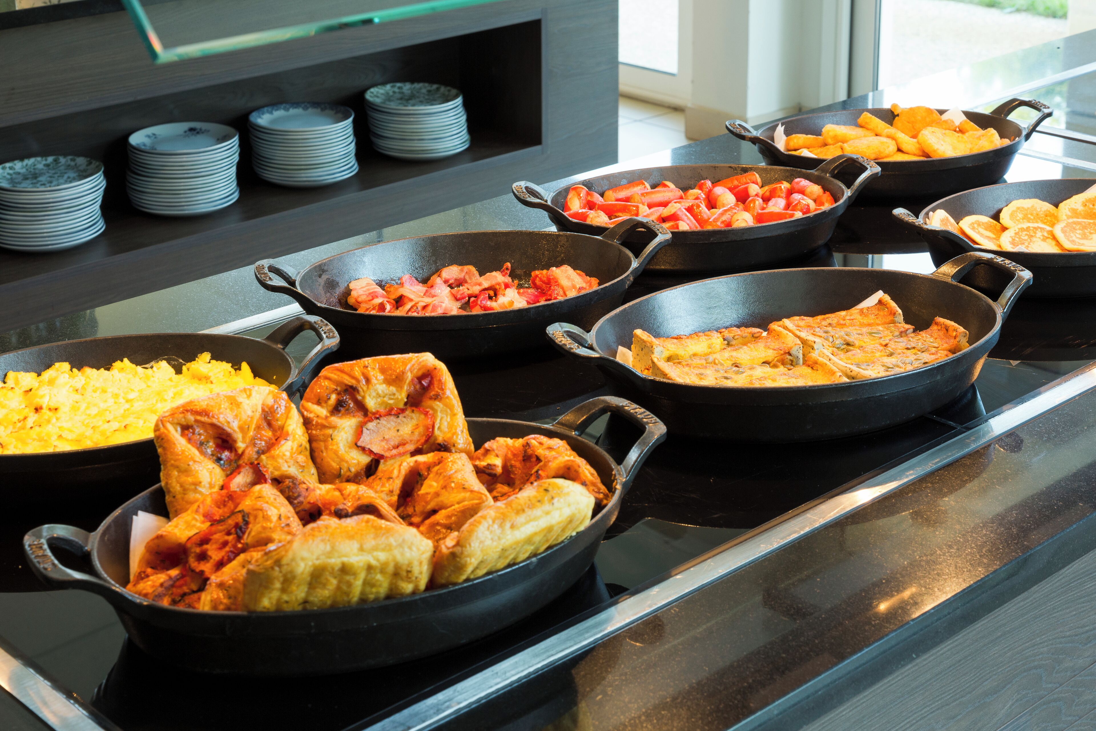 A buffet with various dishes in black pans on a stove.