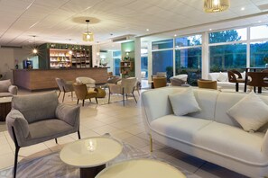 Un moderno vestíbulo de hotel con bar, zona de estar y amplias ventanas.