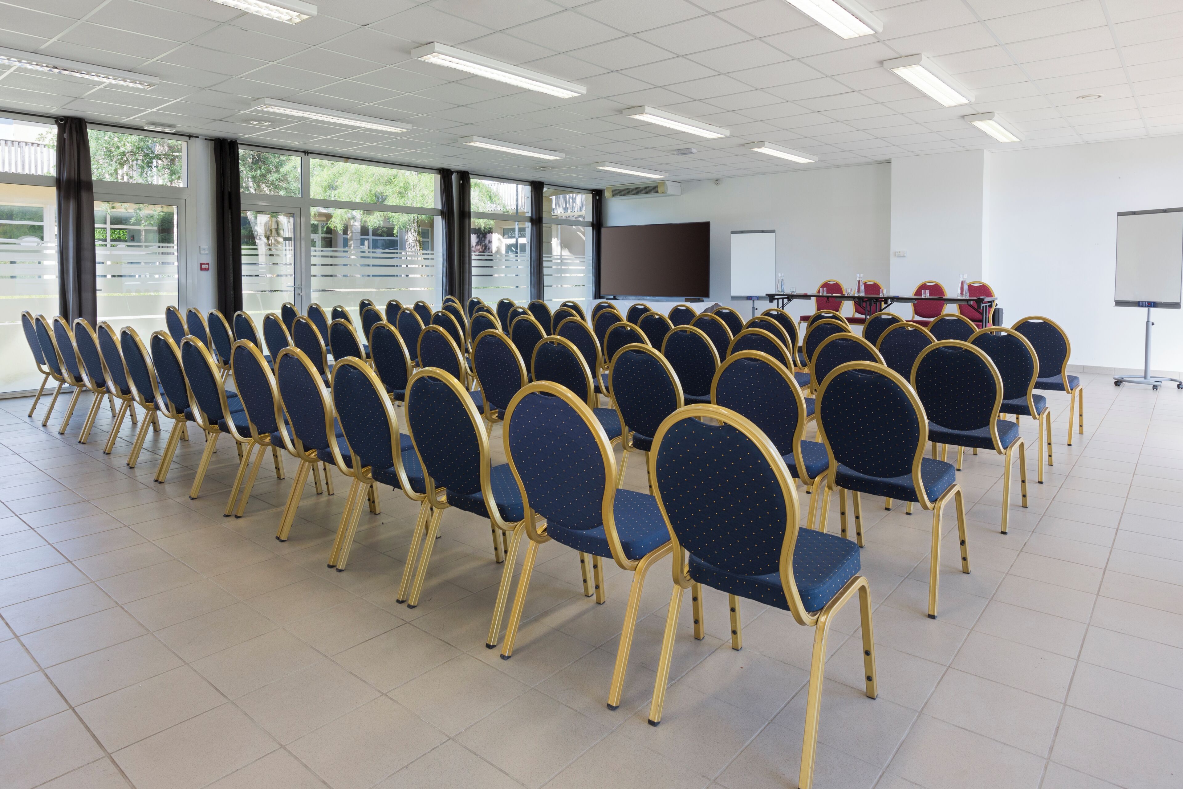 A conference room with rows of blue chairs, a projection screen, and a whiteboard.