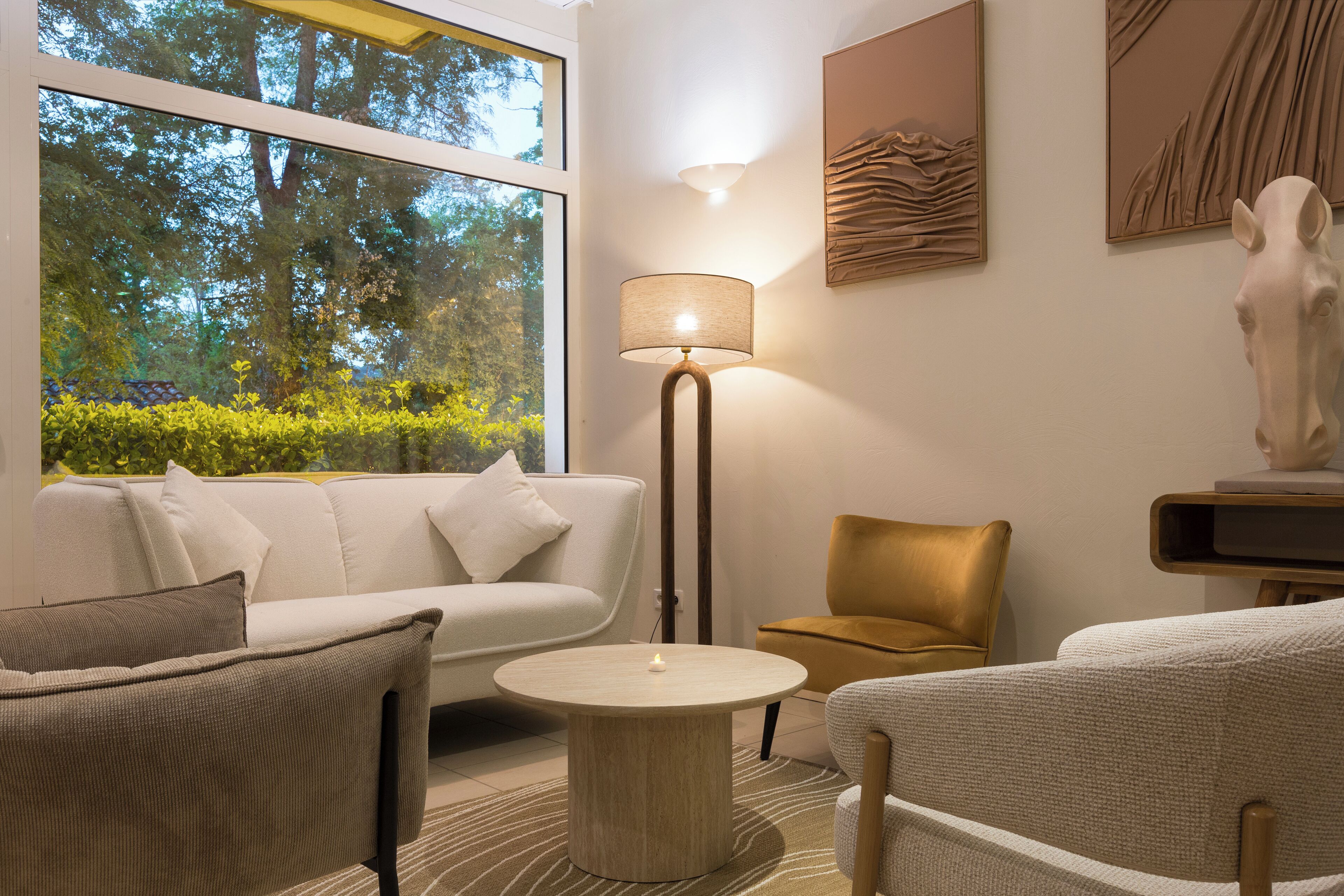 Ein modernes Wohnzimmer mit einer Couch, Sesseln, einem runden Couchtisch, einer Stehlampe und einer Skulptur.