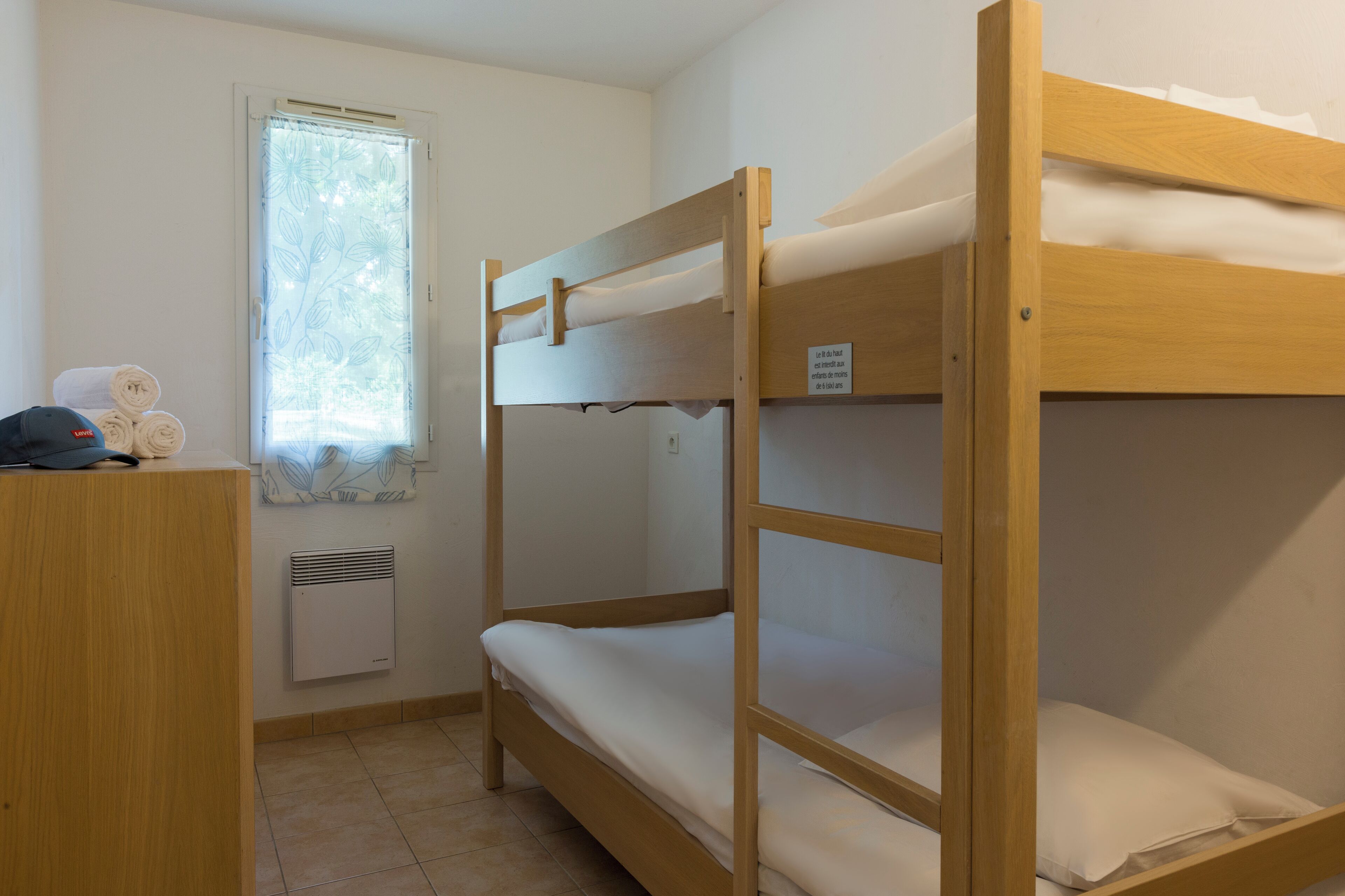 Une chambre avec un lit superposé, une fenêtre, un bureau avec une lampe et un radiateur.