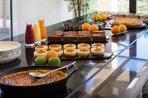 A buffet table with various food items, including desserts and fruits, and a pan of soup.