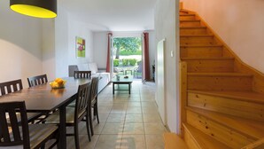 Un espace repas comprenant une table et des chaises, un escalier et, vue depuis une porte, un espace extérieur.