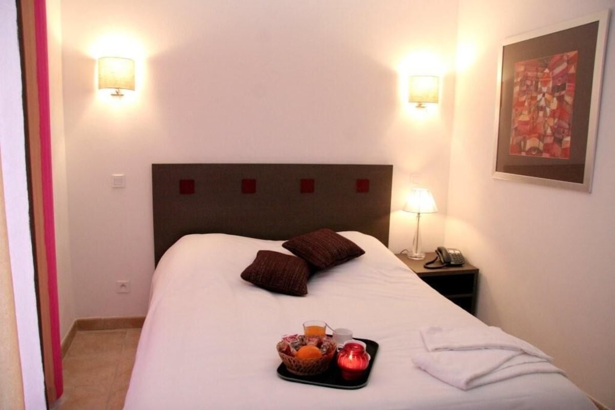 Quarto de hotel com cama, abajures, telefone e bandeja com itens de café da manhã.