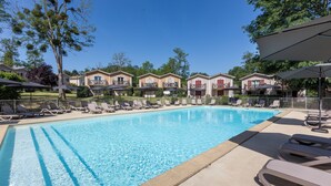 Une piscine entourée de bâtiments dotés de balcons, avec des chaises longues et des parasols, le tout sous un ciel dégagé.
