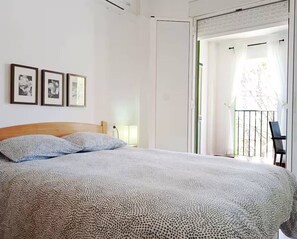 Ein Schlafzimmer mit einem Bett, einem Nachttisch, einer Lampe und einer Tür, die auf einen Balkon führt.