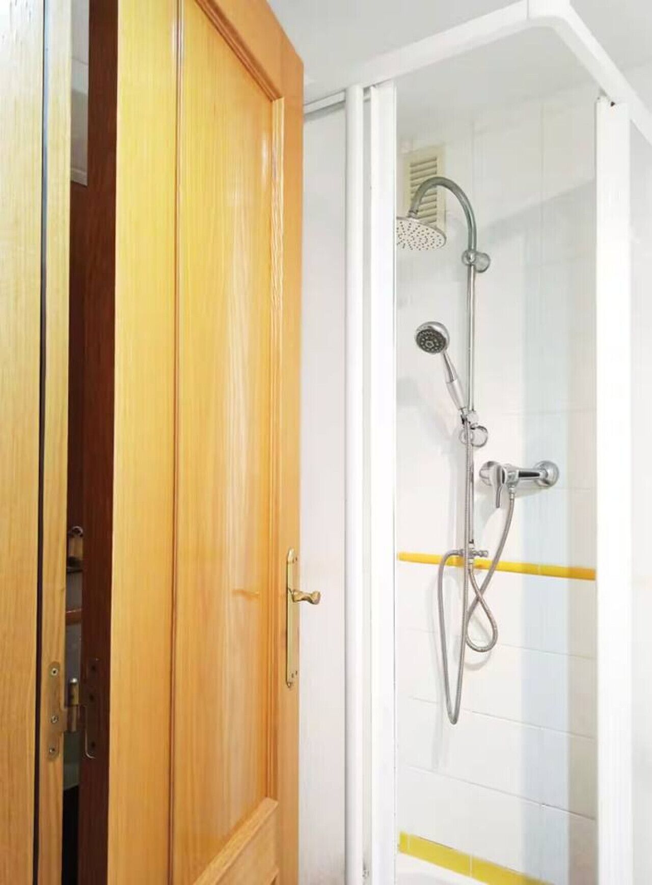 A bathroom with a shower, a wooden door, and white tiled walls.