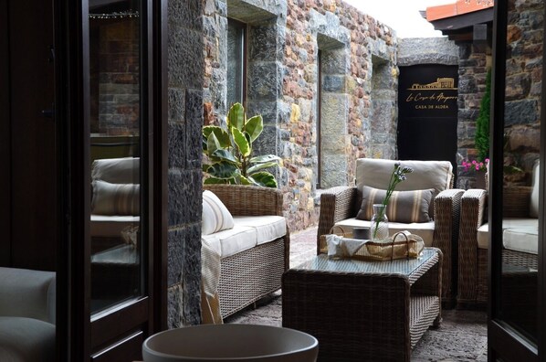 A cozy outdoor seating area with wicker furniture, a stone wall, and a sign reading 'Casa de Aleda.'