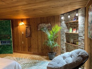 Ein Zimmer mit Holzwänden, einer grünen Tür, einem Blumentopf, einem gepolsterten Sessel und einer Steinwand mit Bücherregalen.