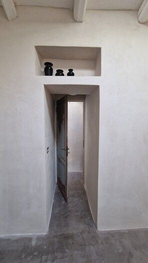 A narrow hallway with a door at the end, a small shelf above it, and a light switch on the wall. - Casa Lureca (Syracuse)