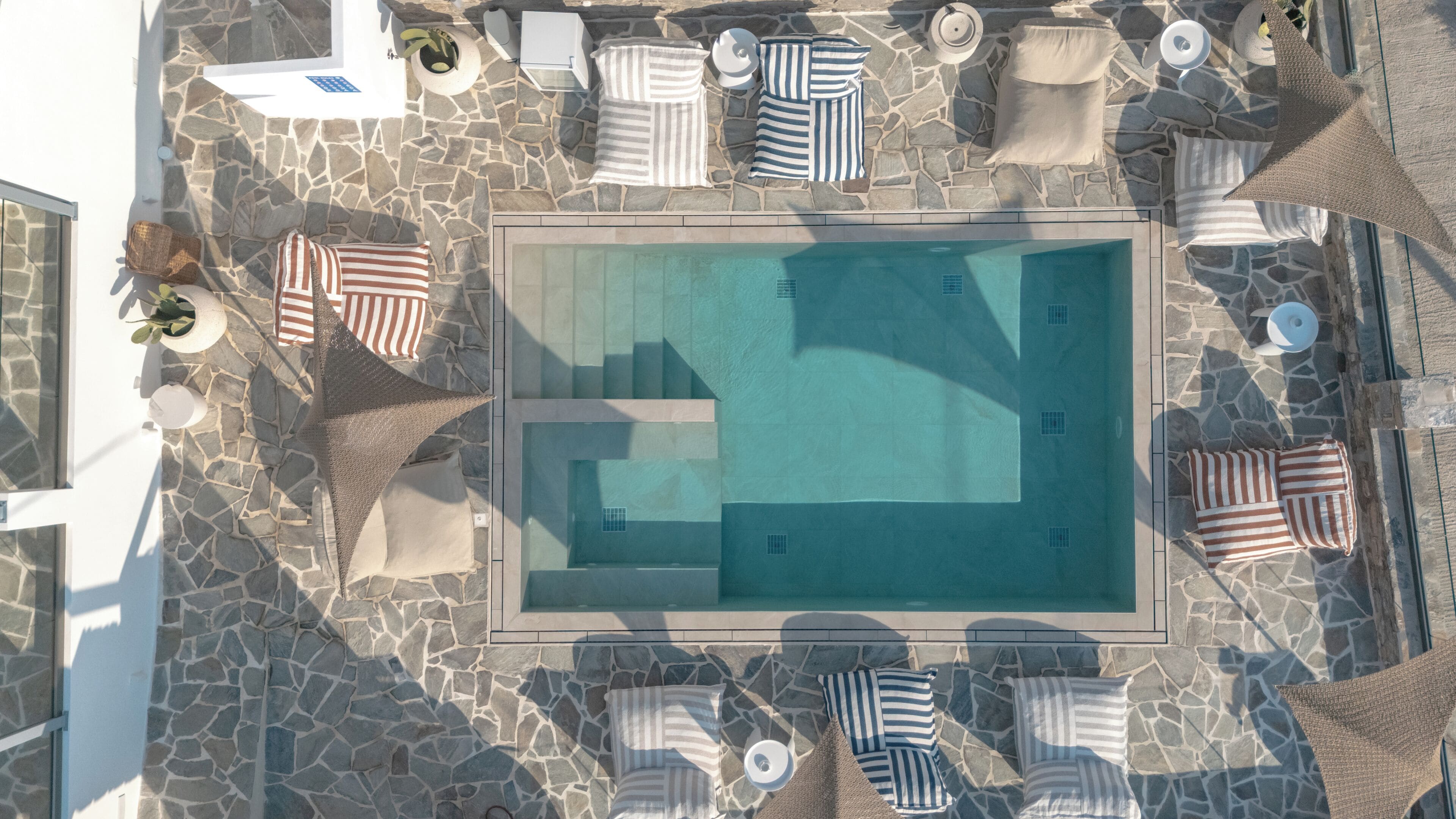 An aerial view of a pool area with stone flooring, lounge chairs, and umbrellas.