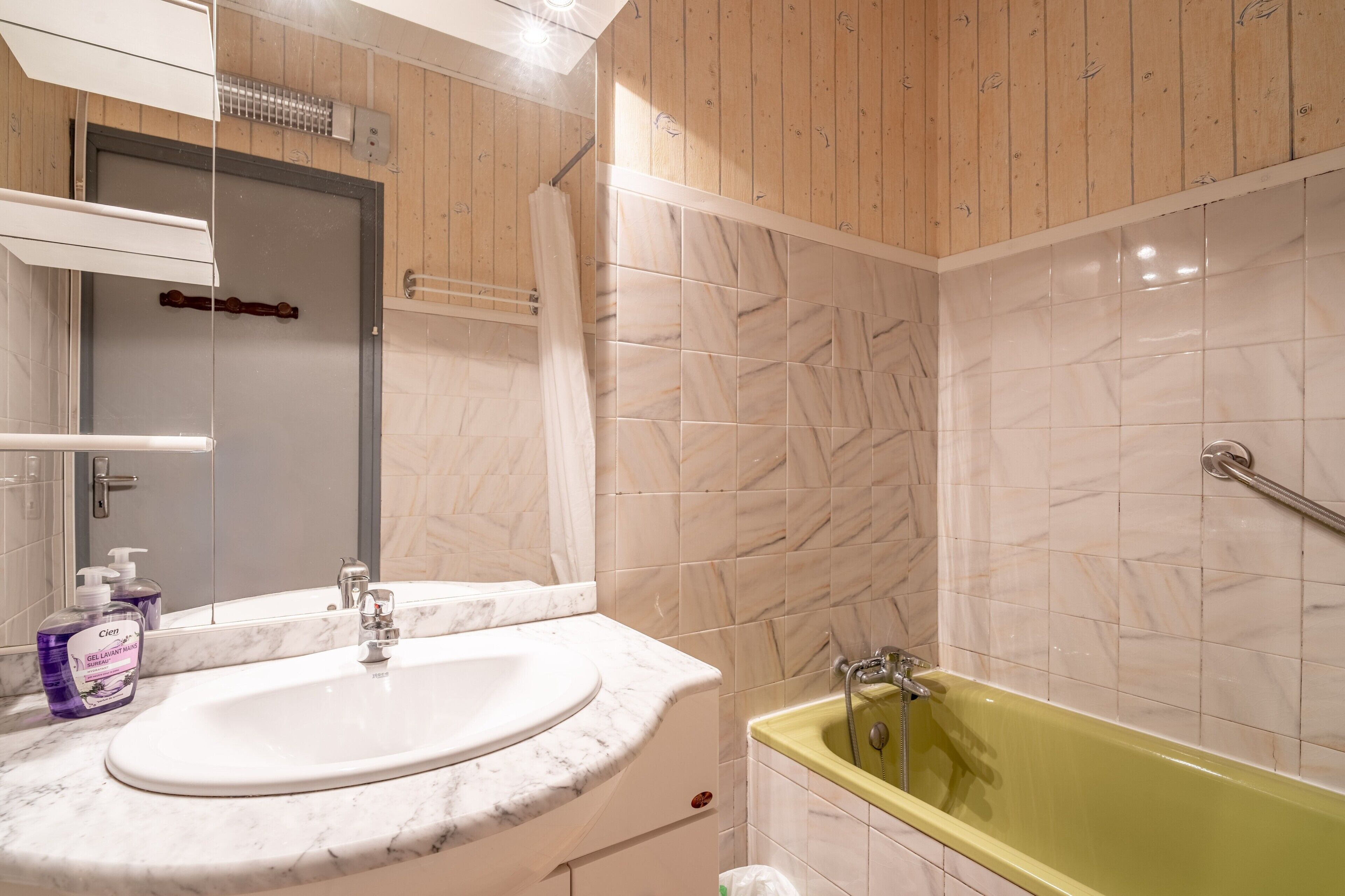 Een badkamer met een wit wastafel, een groen bad en een houten wand.
