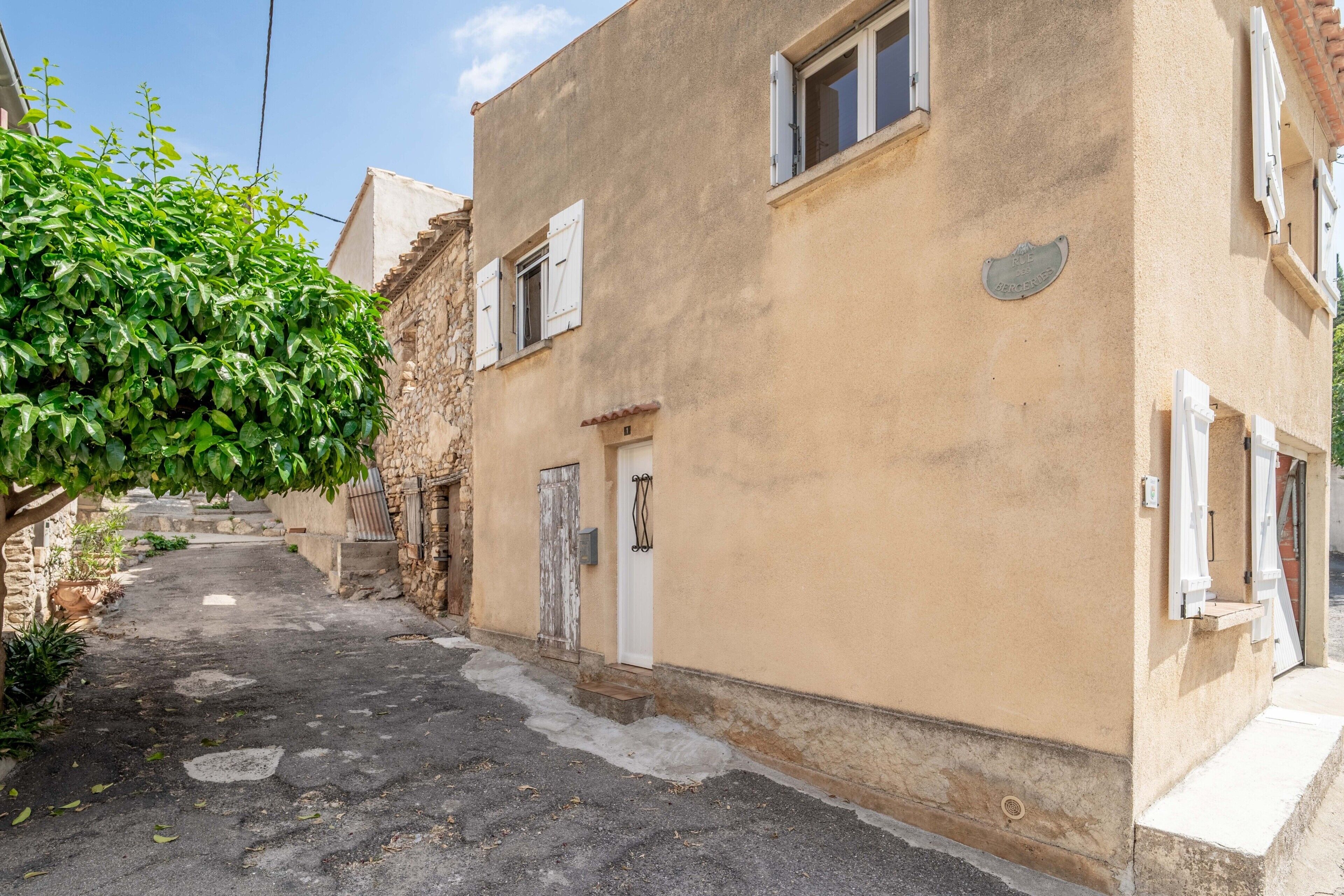 A narrow street with a building featuring a stone facade, a white door, and a small window.