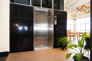 An elevator in a lobby with black walls, potted plants, and a wooden table. - Siantar Hotel Parapat (Medan)