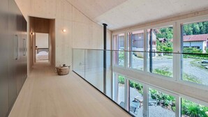 Interior moderno com piso de madeira, guarda-corpo de vidro e vista para uma área residencial.